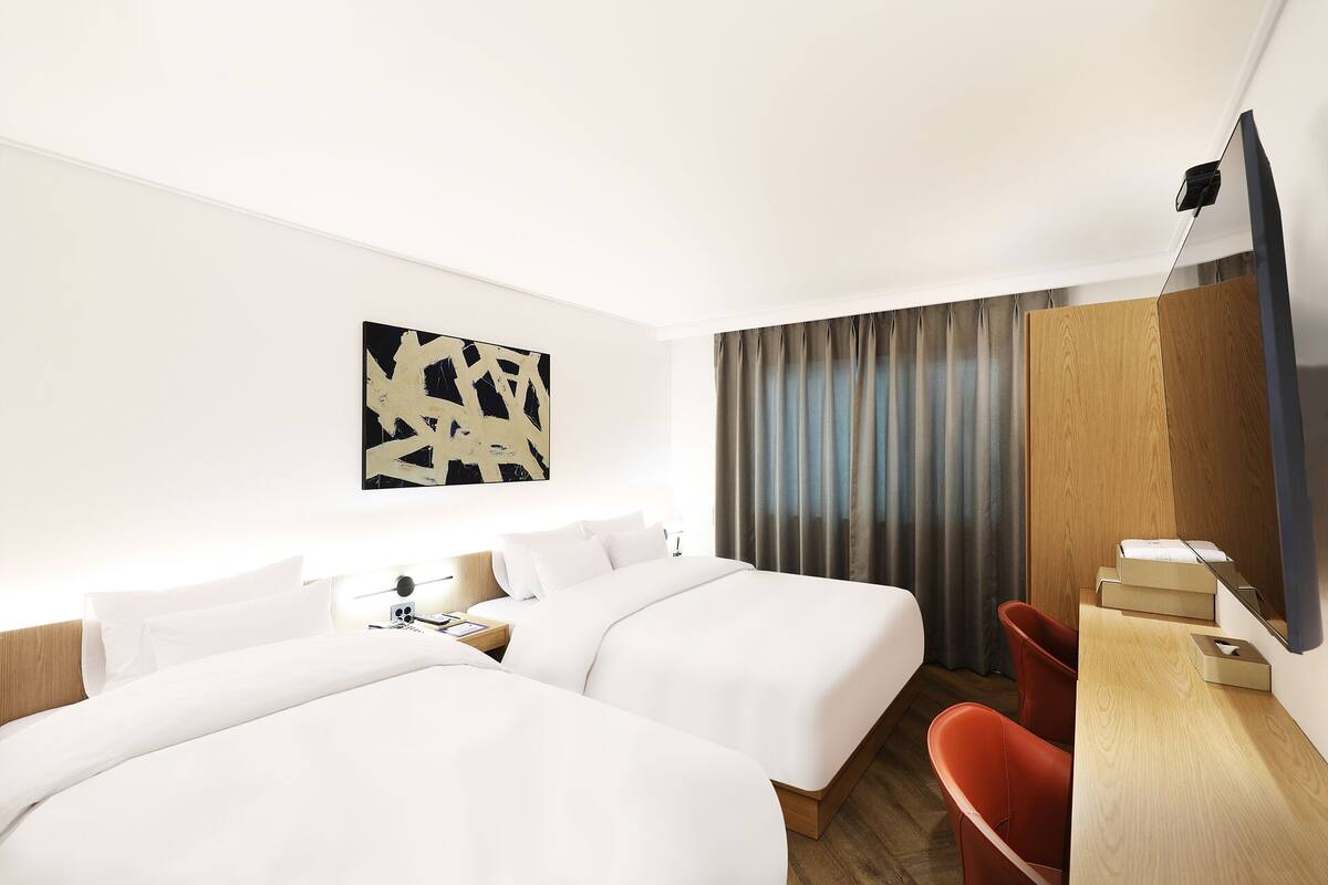 Une chambre d’hôtel avec deux lits, un bureau avec une chaise, une télévision et un grand tableau abstrait accroché au mur.