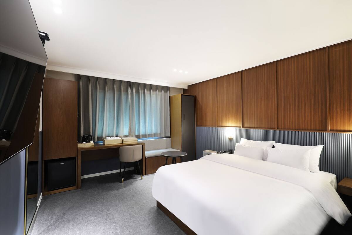 Une chambre d’hôtel avec un grand lit, un bureau avec une chaise, une petite table et une armoire.