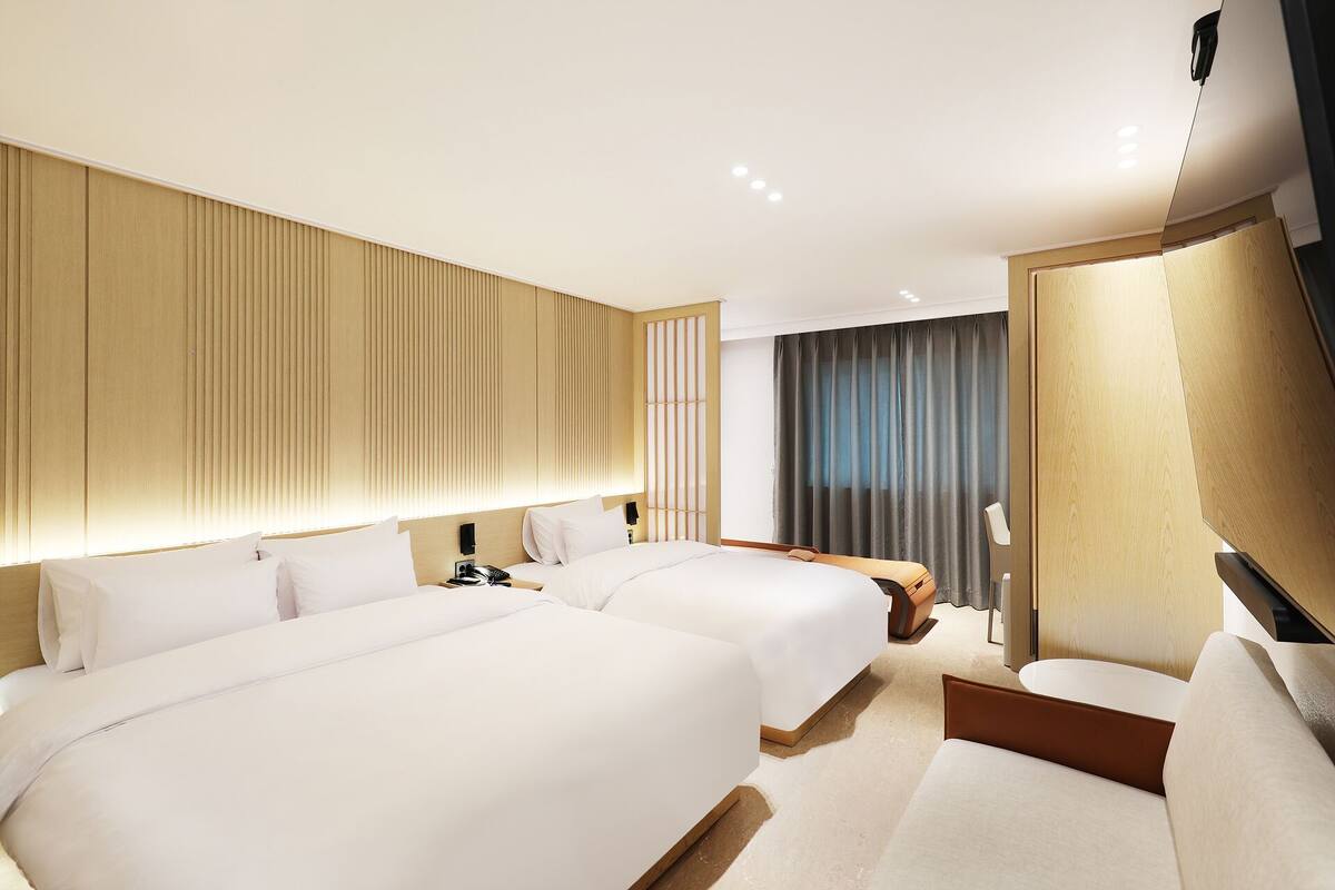 Une chambre d’hôtel avec deux lits, un bureau, une chaise et une grande fenêtre avec des rideaux.