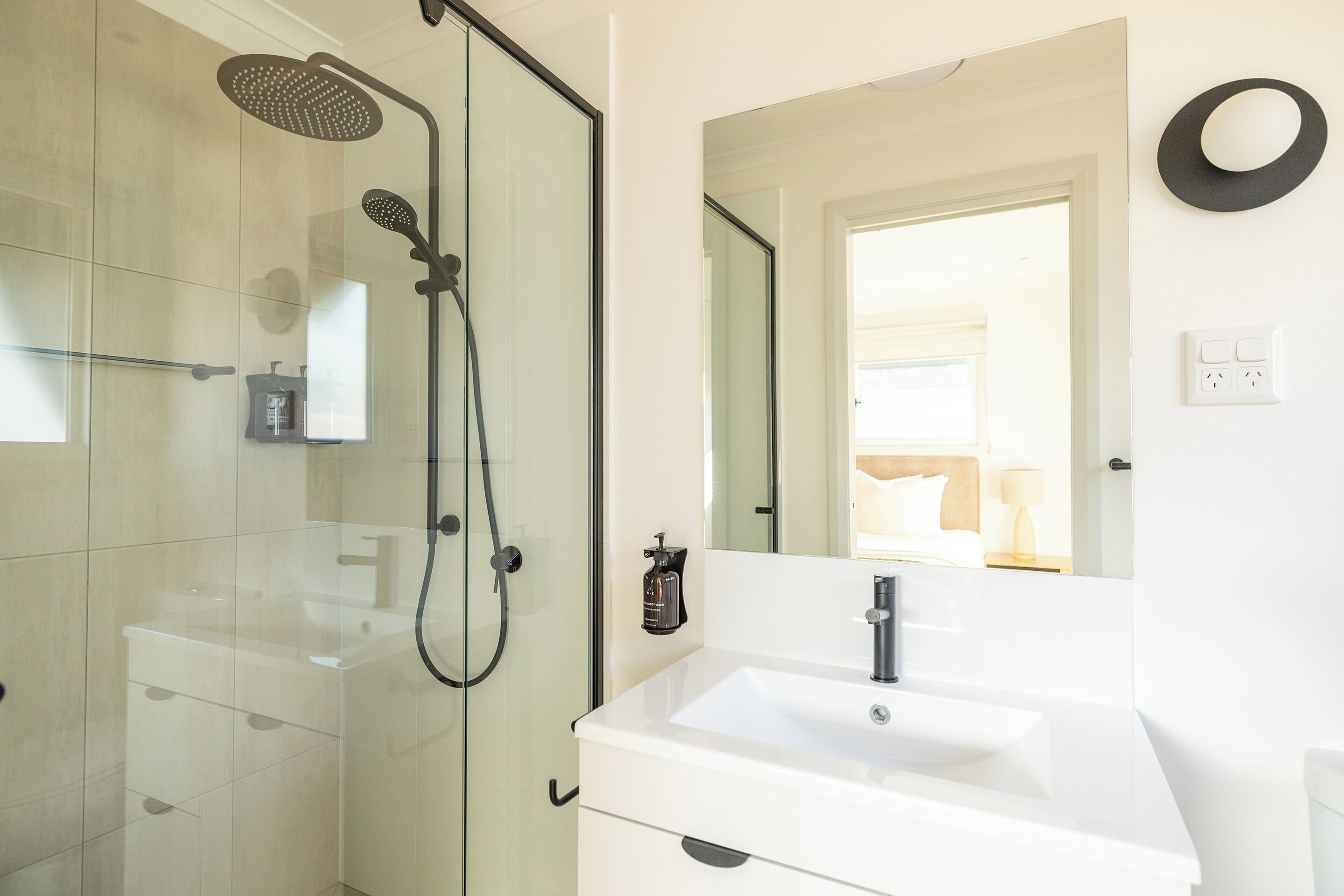 Un baño moderno con ducha envuelta en vidrio, un lavamanos blanco y un espejo.