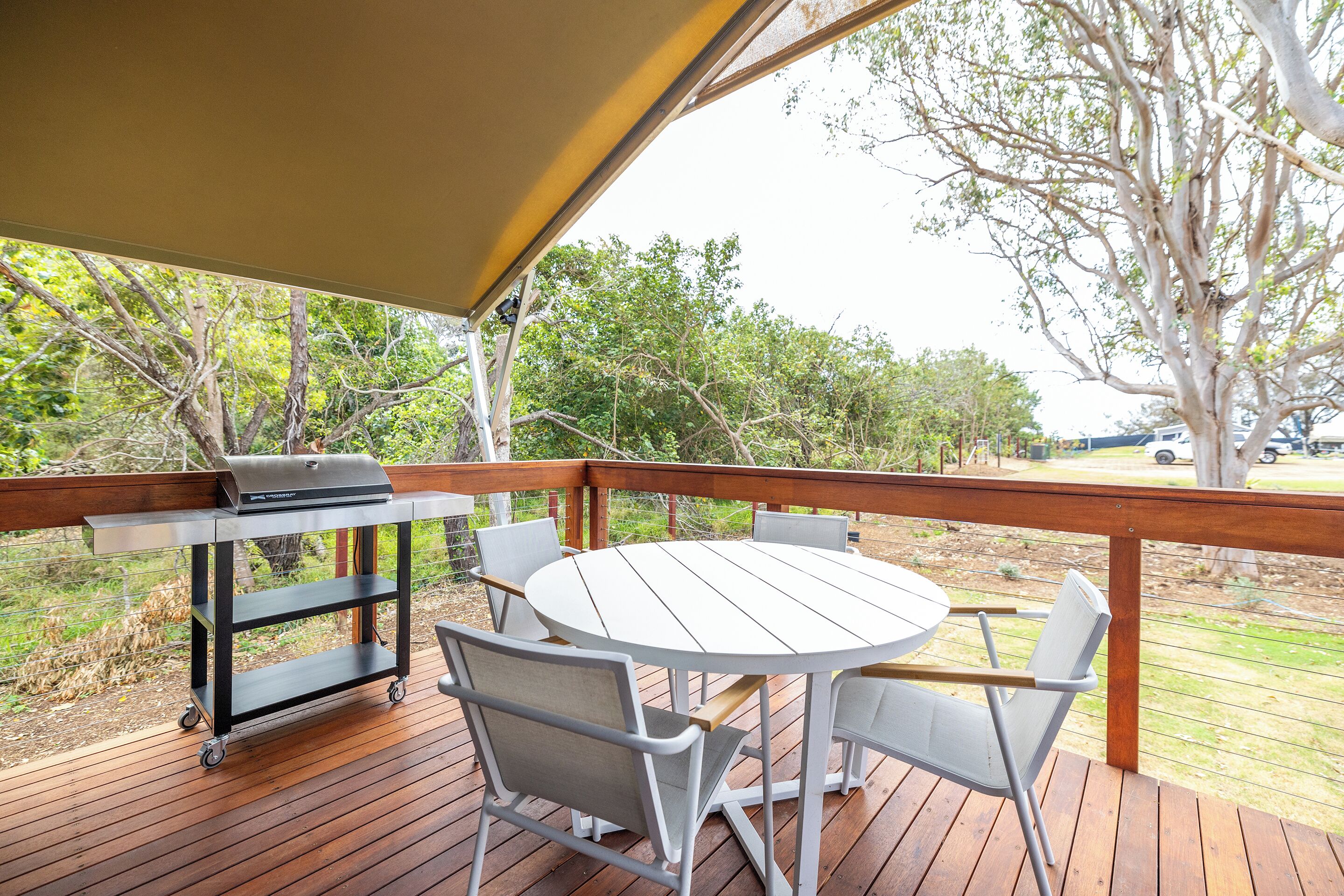 A wooden deck with a round table and chairs, a grill, and a covered area.
