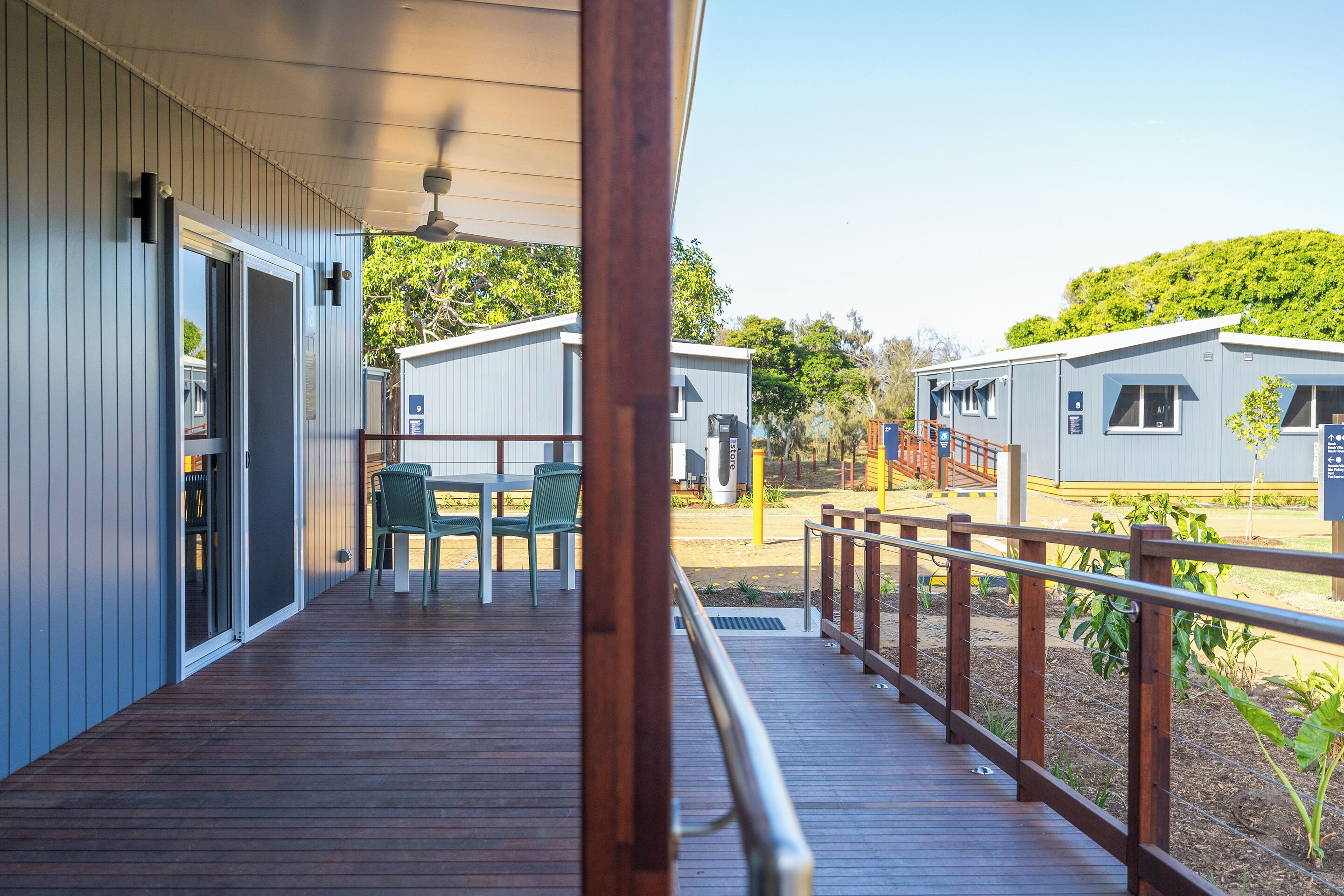 A wooden deck with a railing, a table with chairs, and a building with a door and windows.