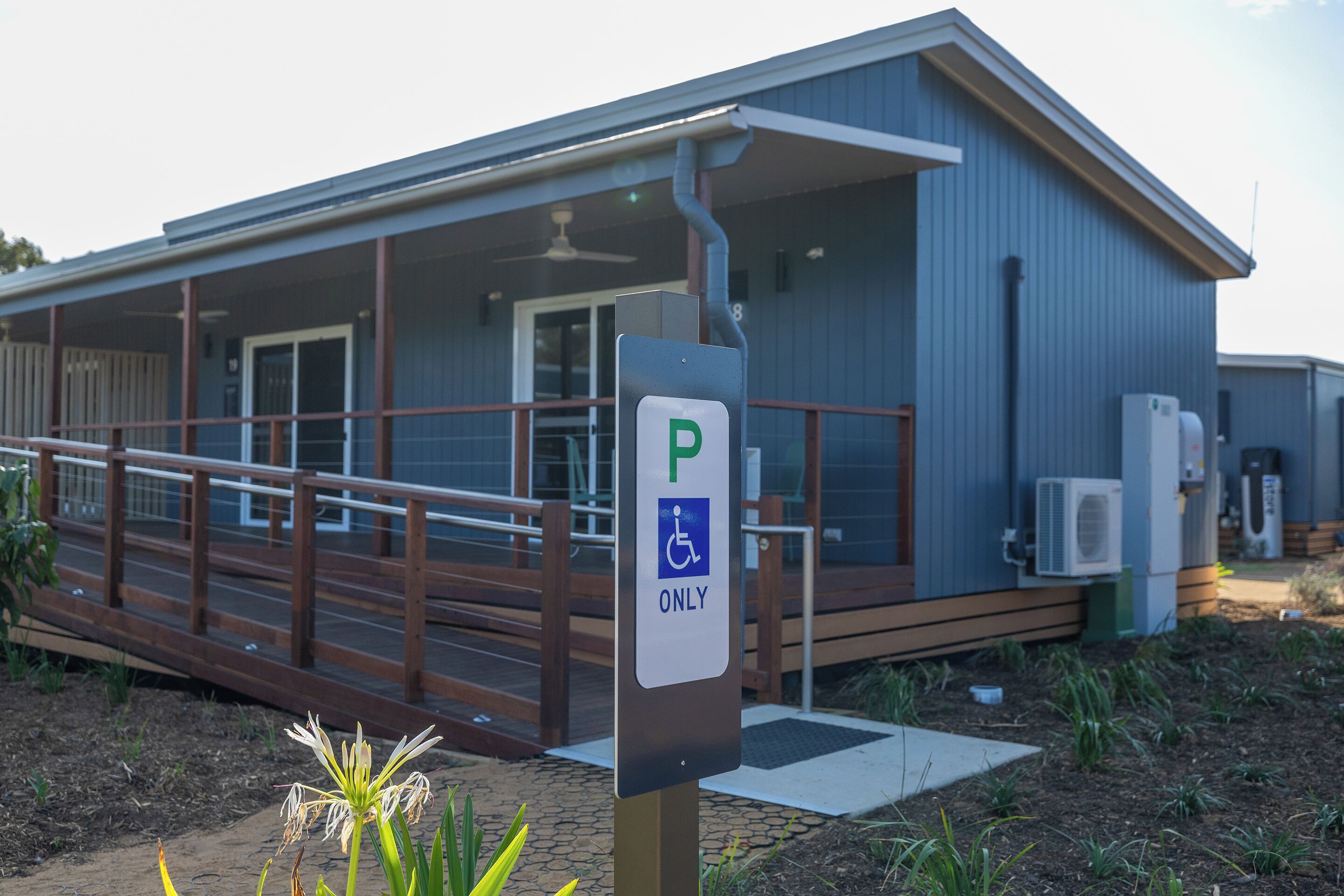 A building with a wheelchair-accessible parking sign, a covered outdoor area with a wooden deck, and an air conditioning unit.
