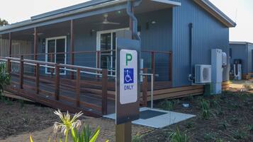 A building with a wheelchair-accessible parking sign, a covered outdoor area with a wooden deck, and an air conditioning unit.