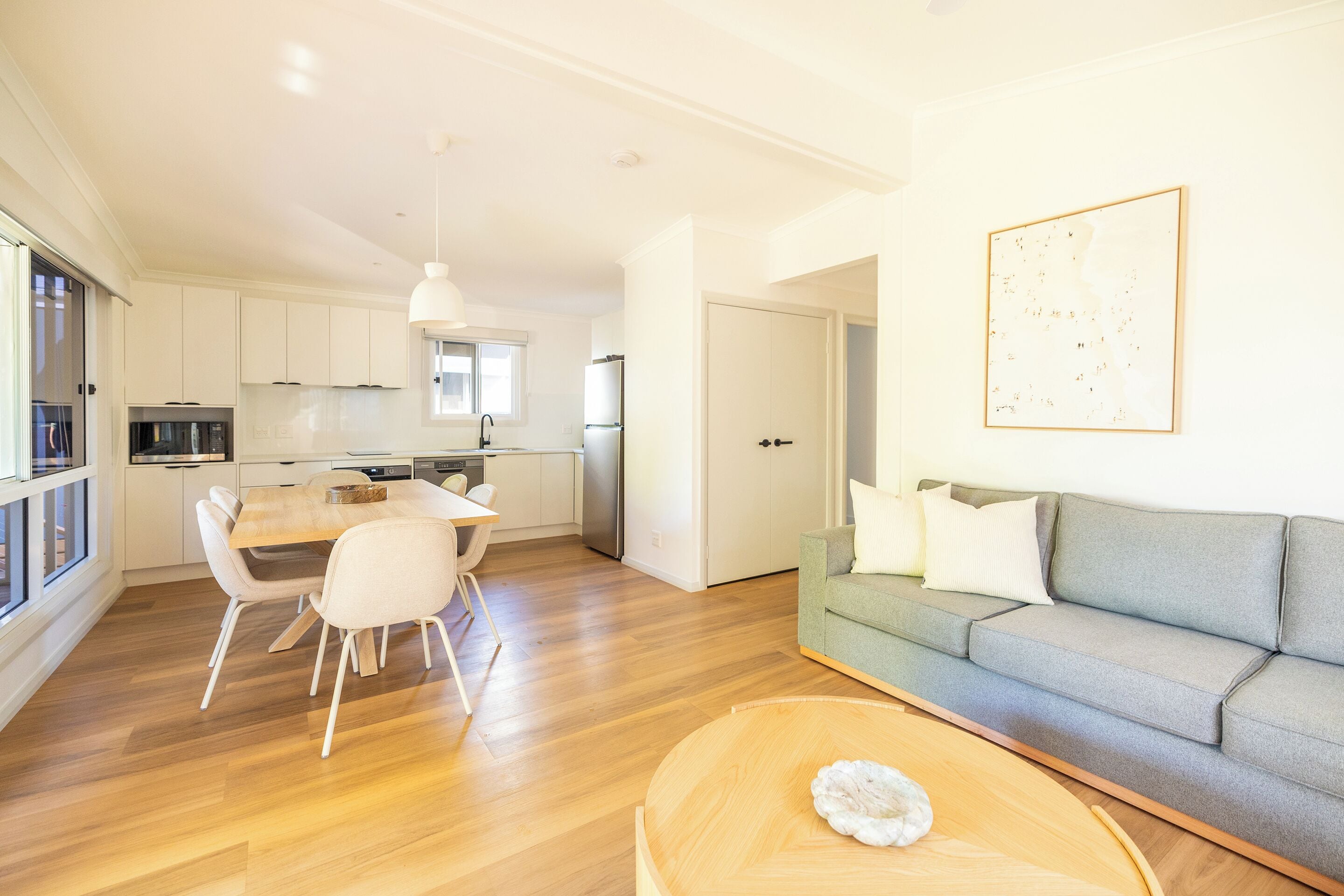 Una sala de estar moderna con un sofá gris, una mesa de centro de madera y un comedor con una mesa y sillas blancas.