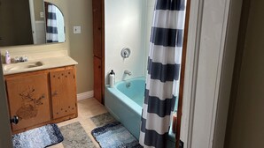 Ein Badezimmer mit einem Holzbadezimmermöbel, einem Waschbecken, einem Spiegel, einer Badewanne und einer Duschvorhang.