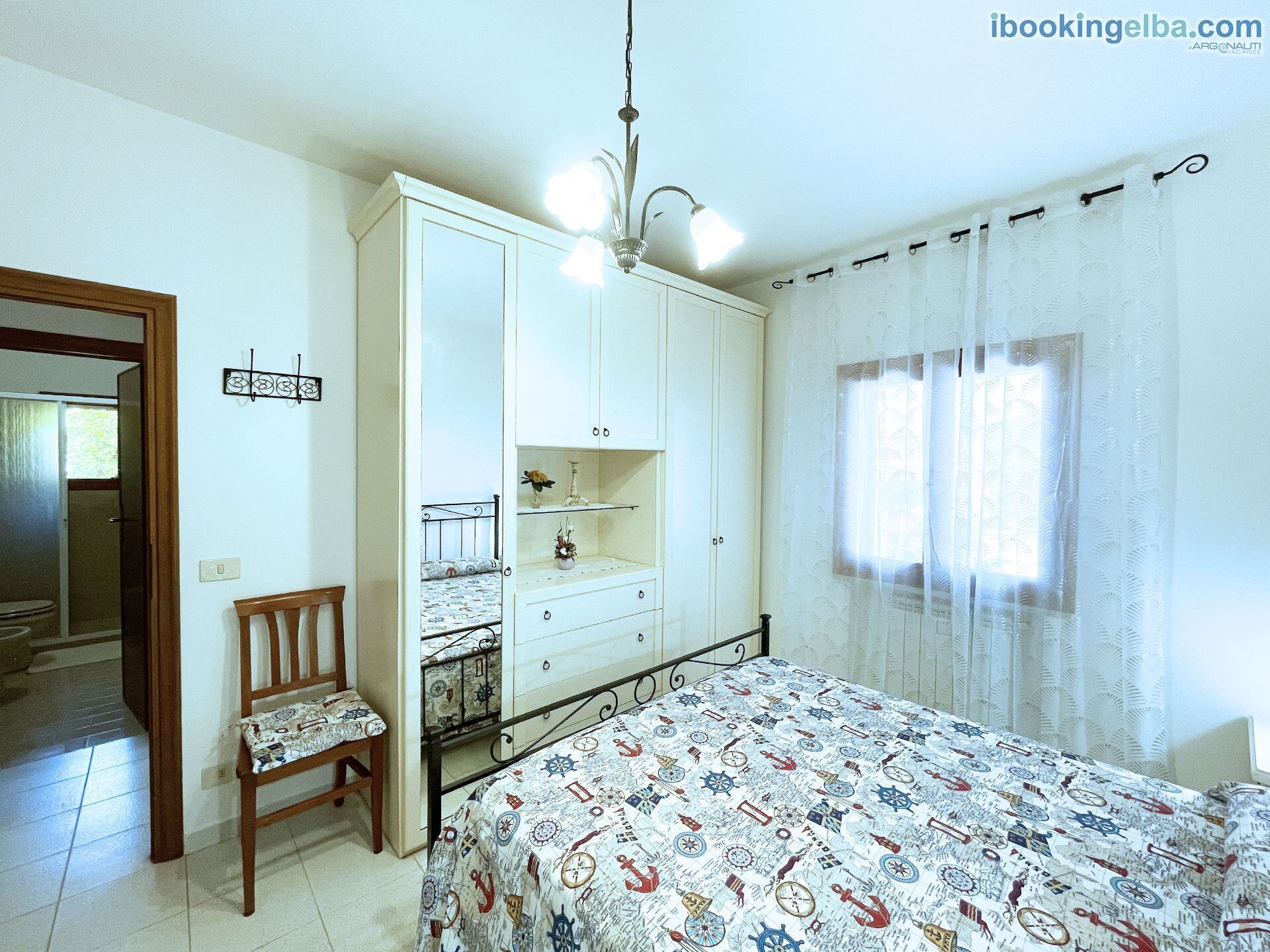 A bedroom with a bed, a chair, a wardrobe, a desk, and a window with curtains.