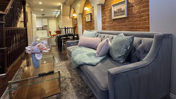 A modern living room with a grey sofa, a glass coffee table, and a patterned rug. There is a staircase with wooden railings and a dining area in the background. - Spacious 3 bedroom Townhome in the heart of Baltimore  (Baltimore)
