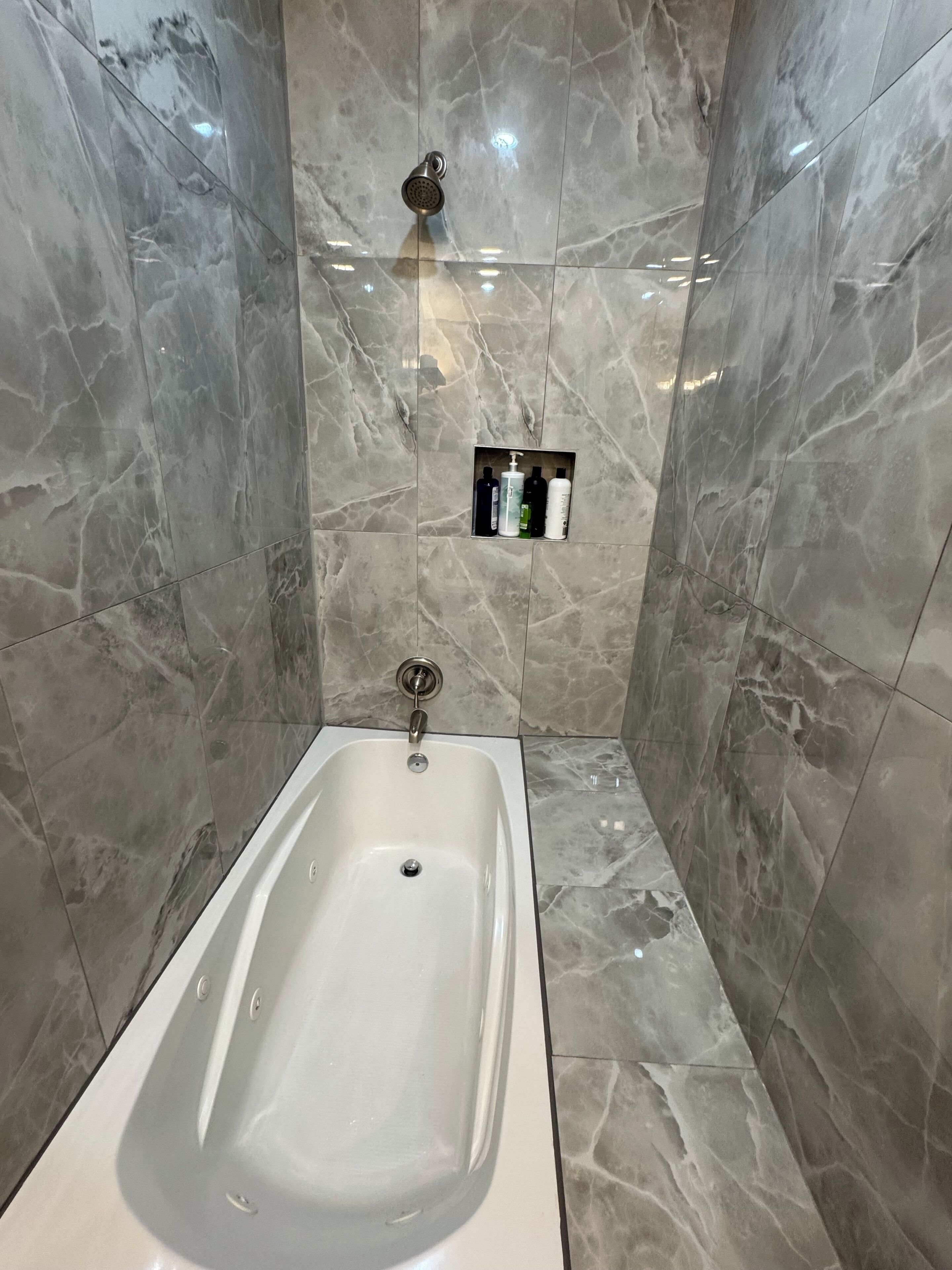 Une salle de bain moderne avec une baignoire sur pieds, des murs en marbre et une étagère intégrée pour les articles de toilette.