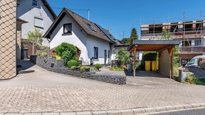 A residential area with a paved driveway, a white house with a sloped roof, and a construction site in the background. - Holiday Home 'Eiffelperle' with Private Terrace, Garden, Infrared Sauna & Wi-Fi (Kaisersesch)