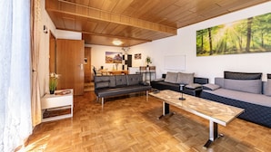 A modern living room with a wooden ceiling, a sofa, a coffee table, and a dining area in the background. - Holiday Home 'Eiffelperle' with Private Terrace, Garden, Infrared Sauna & Wi-Fi (Kaisersesch)