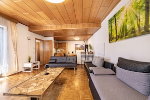 Una sala de estar moderna con techo de madera, un sofá, una mesa de centro y un cuadro de un bosque.