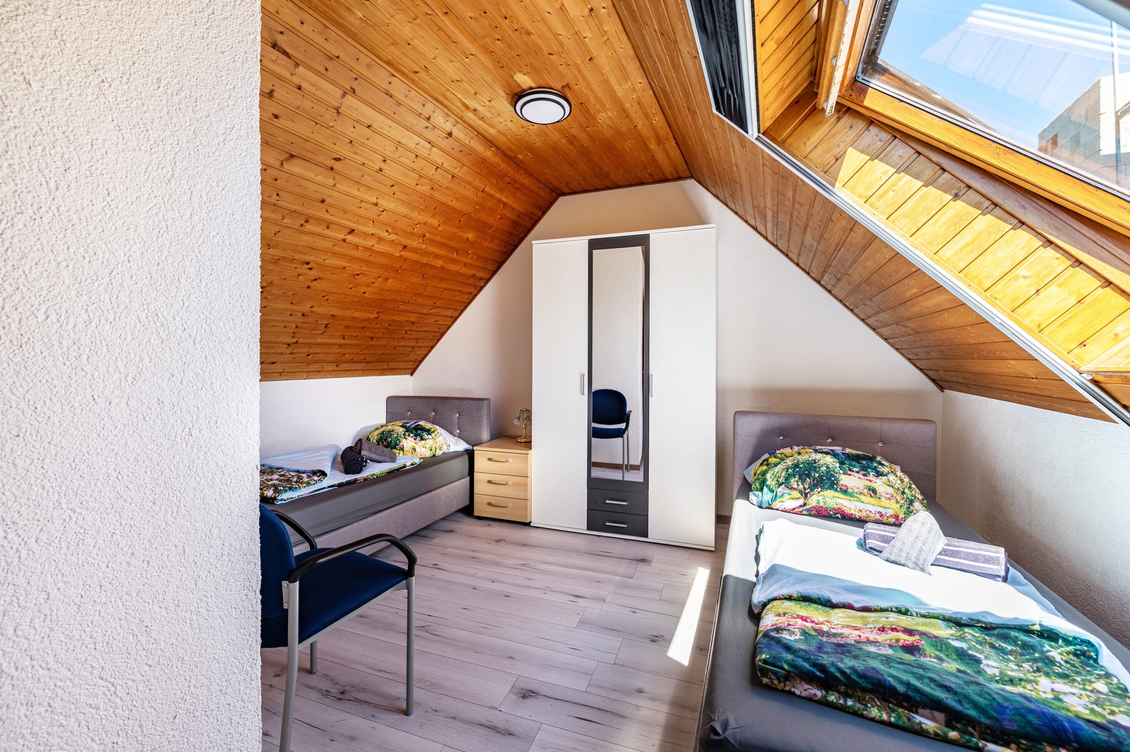 A bedroom with a sloped ceiling, a bed, a desk, a chair, and a wardrobe.