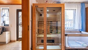 A room with a wooden cabinet, a bed with a blue and white bedspread, a window with a curtain, and a radiator. - Holiday Home 'Eiffelperle' with Private Terrace, Garden, Infrared Sauna & Wi-Fi (Kaisersesch)