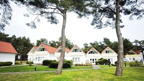 A row of white houses with red roofs, arranged in a straight line, surrounded by well-maintained lawns and trees.