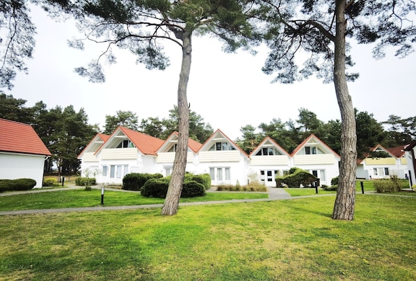 A row of white houses with red roofs, arranged in a straight line, surrounded by well-maintained lawns and trees.
