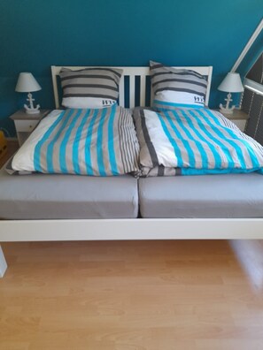 A bed with striped bedding, two bedside tables with lamps, and a blue wall. - Apartment 'Die Blaue Lagune, Hinter Den Dünen' with Balcony and Wi-Fi (Prerow)