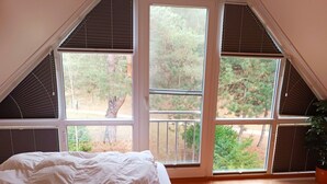 A bedroom with a large window, a bed, and a view of trees.