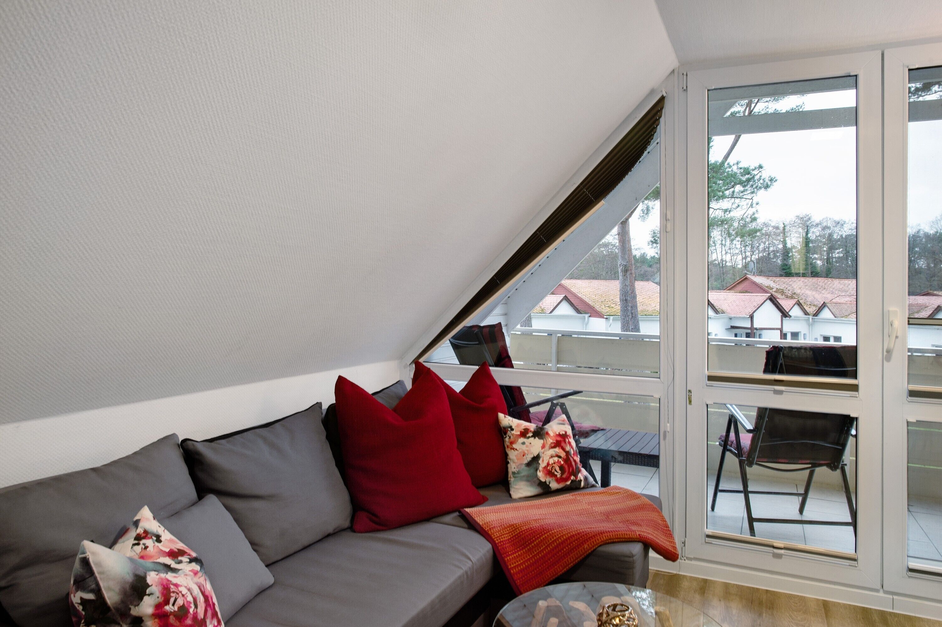 A modern interior with a grey sofa, red cushions, and a glass door leading to an outdoor balcony.