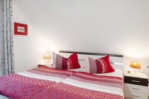 Un lit bien fait, avec une literie à motifs, une table de chevet avec une lampe et un tableau encadré au mur.