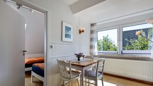 A room with a bed, a table with chairs, a window with a view of greenery, and a radiator. - Apartment 'Jule' with Shared Terrace, Shared Garden and Wi-Fi (Pellworm)