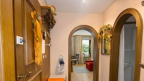 Un pasillo con puerta de madera, zapatero, perchero, alfombra y un arco que da a un balcón.