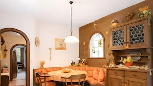 Un rincón comedor acogedor con una mesa redonda, sillas de madera y un banco. Se observa un aparador de madera con puertas de cristal y una lámpara colgante sobre la mesa.