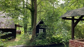A rustic cabin with a thatched roof, surrounded by dense greenery and a small water feature. - Holiday Home 'Ferienhaus Im Spreewald' with Private Terrace, Shared Garden and Wi-Fi (Märkische Heide)