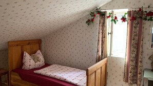 A single wooden bed with floral bedding, a wooden nightstand, a window with floral curtains, and a wall with a floral pattern. - Holiday Home 'Ferienhaus Im Spreewald' with Private Terrace, Shared Garden and Wi-Fi (Märkische Heide)