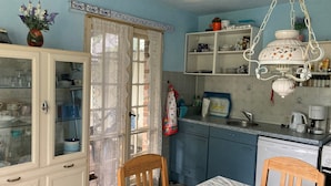 A kitchen with a dining table, chairs, a blue trash bin, a white cabinet with glass doors, and a hanging light fixture. - Holiday Home 'Ferienhaus Im Spreewald' with Private Terrace, Shared Garden and Wi-Fi (Märkische Heide)