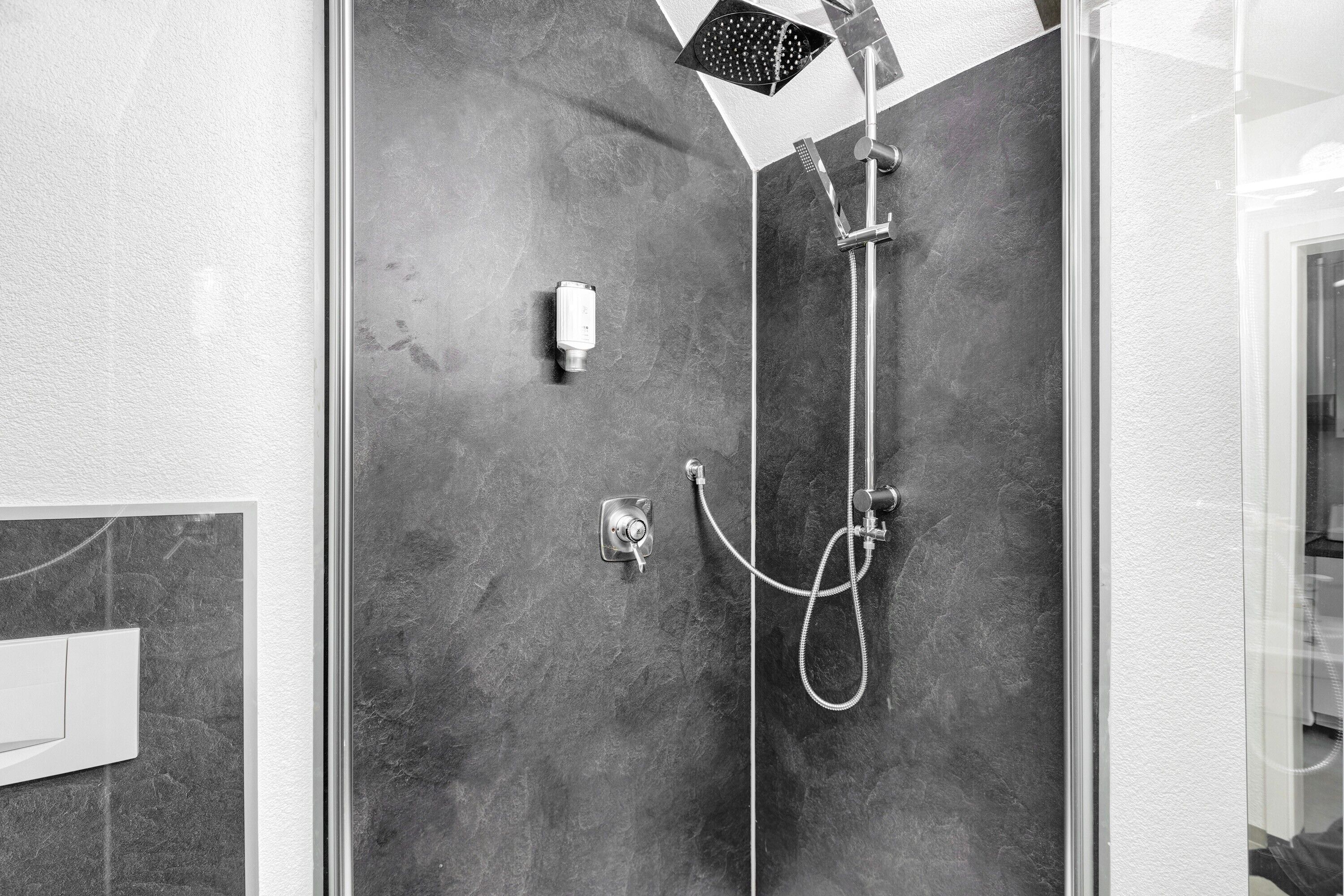 Eine moderne Dusche mit Duschbrause, Wandarmatur und Bedienfeld.