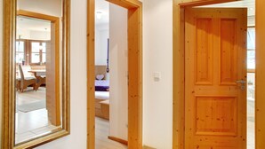A hallway with wooden doors and a mirror reflecting a room with a bed and a chair. - Apartment 'Landhaus Bergkulisse' with Mountain View, Shared Terrace and Wi-Fi (Wallgau)