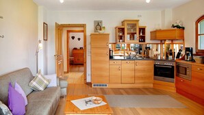 A modern kitchen with wooden cabinets, a dining area with a table, and a living room with a sofa. - Apartment 'Landhaus Bergkulisse' with Mountain View, Shared Terrace and Wi-Fi (Wallgau)