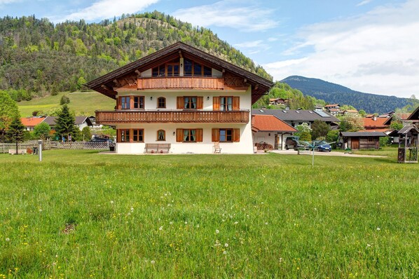 A two-story building with a balcony, surrounded by a grassy field and a mountainous backdrop.