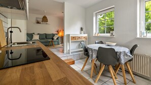A modern kitchen with a wooden countertop and integrated appliances, a dining area with a round table and chairs, and a view of greenery through a large window. - Apartment 'Ferienwohnung Block' with Private Terrace, Private Garden and Wi-Fi (Glücksburg (Ostsee))