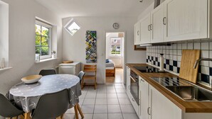 A compact kitchen with a dining area, a clock, and a view into another room. - Apartment 'Ferienwohnung Block' with Private Terrace, Private Garden and Wi-Fi (Glücksburg (Ostsee))