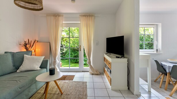 A modern living room with a sofa, TV, dining area, and large windows. - Apartment 'Ferienwohnung Block' with Private Terrace, Private Garden and Wi-Fi (Glücksburg (Ostsee))
