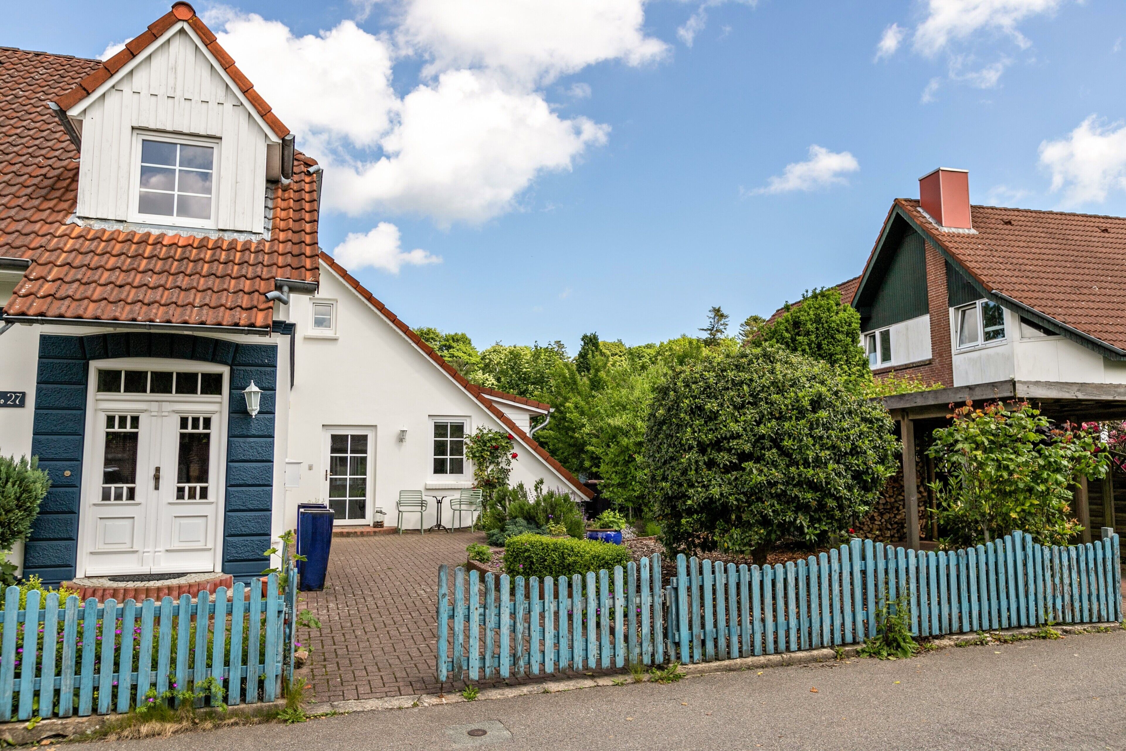A two-story house with a red-tiled roof, a white door, and a blue picket fence.