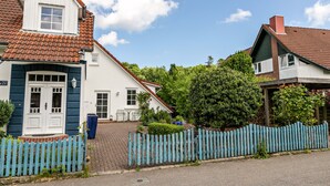 A two-story house with a red-tiled roof, a white door, and a blue picket fence. - Apartment 'Ferienwohnung Block' with Private Terrace, Private Garden and Wi-Fi (Glücksburg (Ostsee))