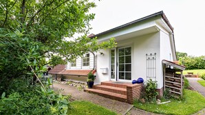 A white building with a brick foundation, a tiled roof, and a small porch. - Apartment 'Ferienwohnung Block' with Private Terrace, Private Garden and Wi-Fi (Glücksburg (Ostsee))