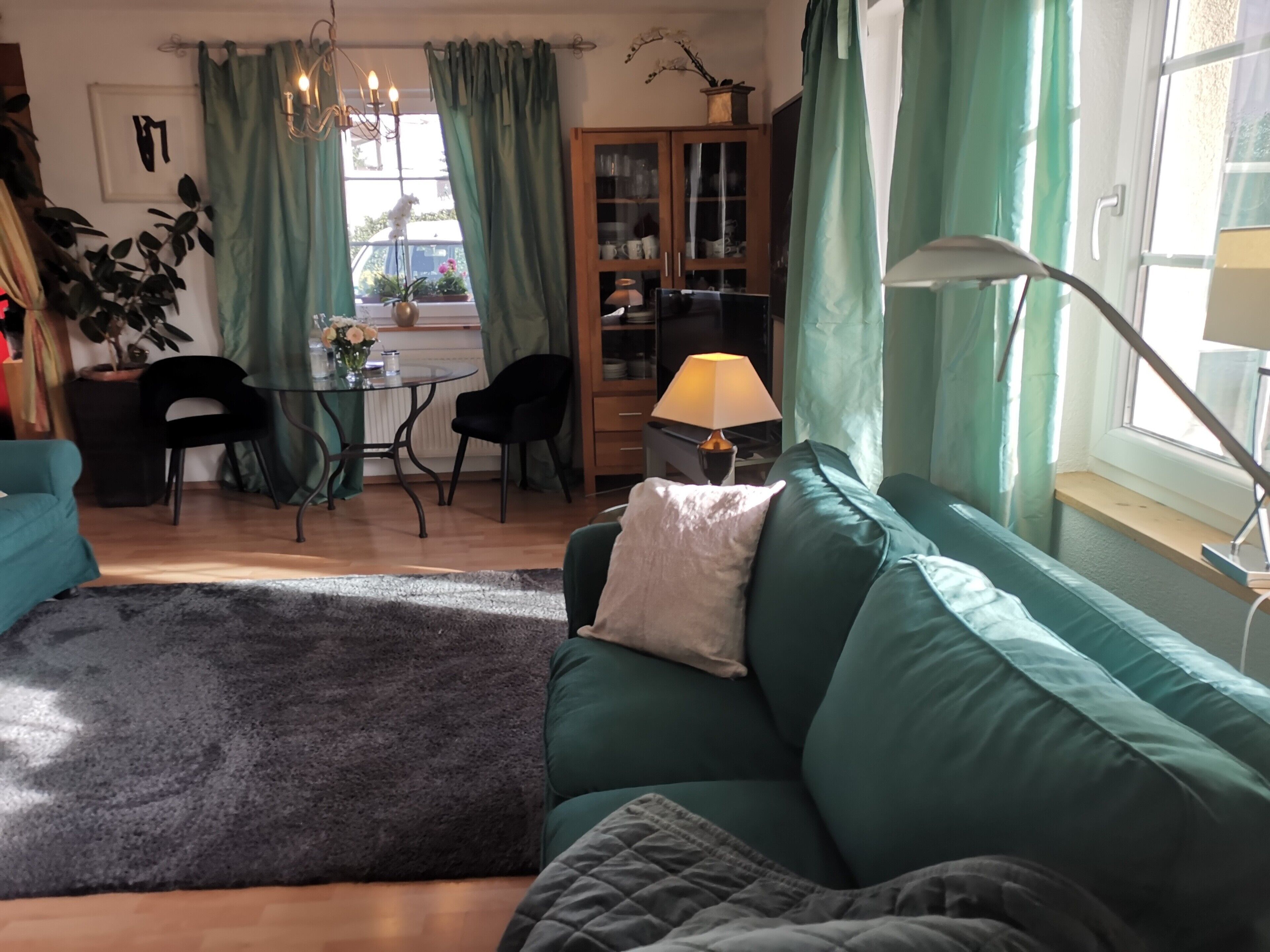 A cozy living room with a green sofa, a coffee table, and a dining area with chairs and a lamp.