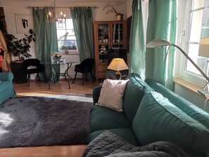 A cozy living room with a green sofa, a coffee table, and a dining area with chairs and a lamp.