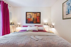 A hotel room with a bed, two bedside lamps, a painting on the wall, and a poster.
