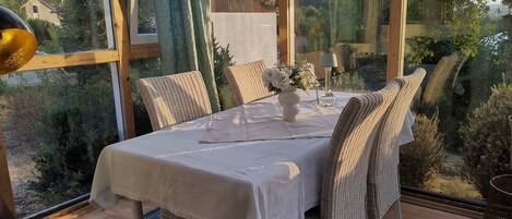 A dining area with a table set for two, wicker chairs, a vase with flowers, and a lamp.