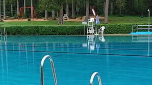 En swimmingpool med metalstiger, et rødt gyngestativ og en rutchebane i baggrunden.