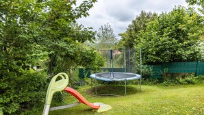 En trampolin omgivet af et grønt hegn og frodig beplantning.