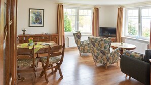 A dining area with a wooden table and chairs, a television, and a sofa. - Holiday Home 'Eiderblick' with Private Terrace, Private Garden and Wi-Fi (Borgstedt)