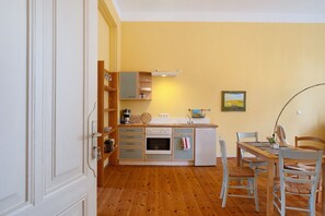 Eine kompakte Küche mit Einbauofen, Spüle und kleinem Kühlschrank. Es gibt einen Esstisch mit Stühlen und ein Bild an der Wand.