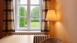 Een kamer met raam, gordijnen, lamp en een radiator.