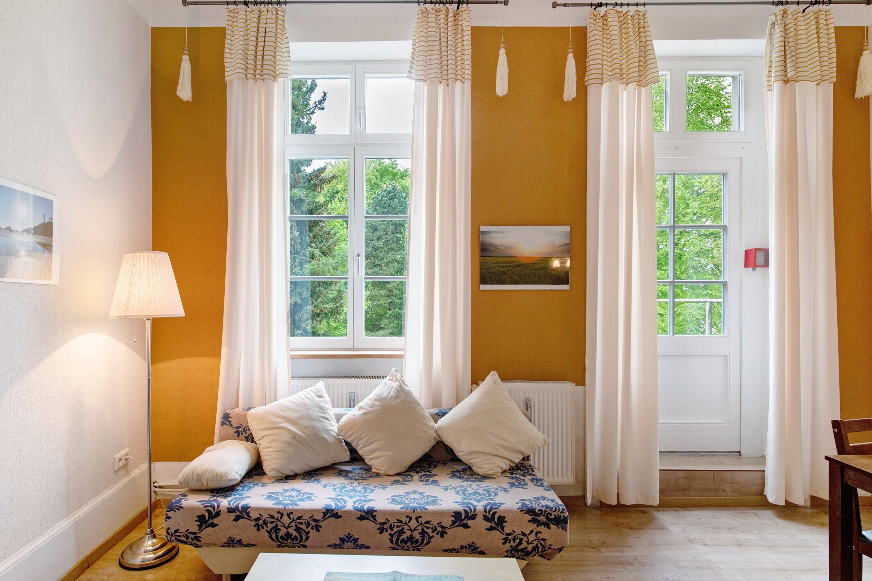 A room with a bed, a floor lamp, a radiator, and two windows with curtains.